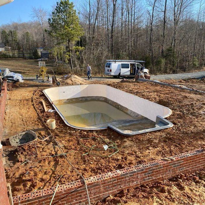 Backyard construction site with a partially filled in-ground pool and workers nearby