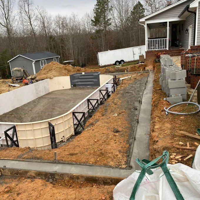 Backyard construction site with a small pool, concrete walls, cinder blocks, and a house porch