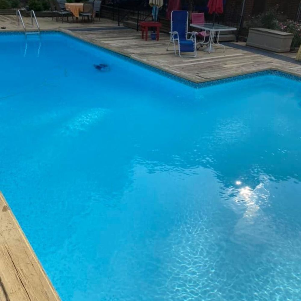 Blue swimming pool beside a wooden deck with lounge chairs and tables in the background