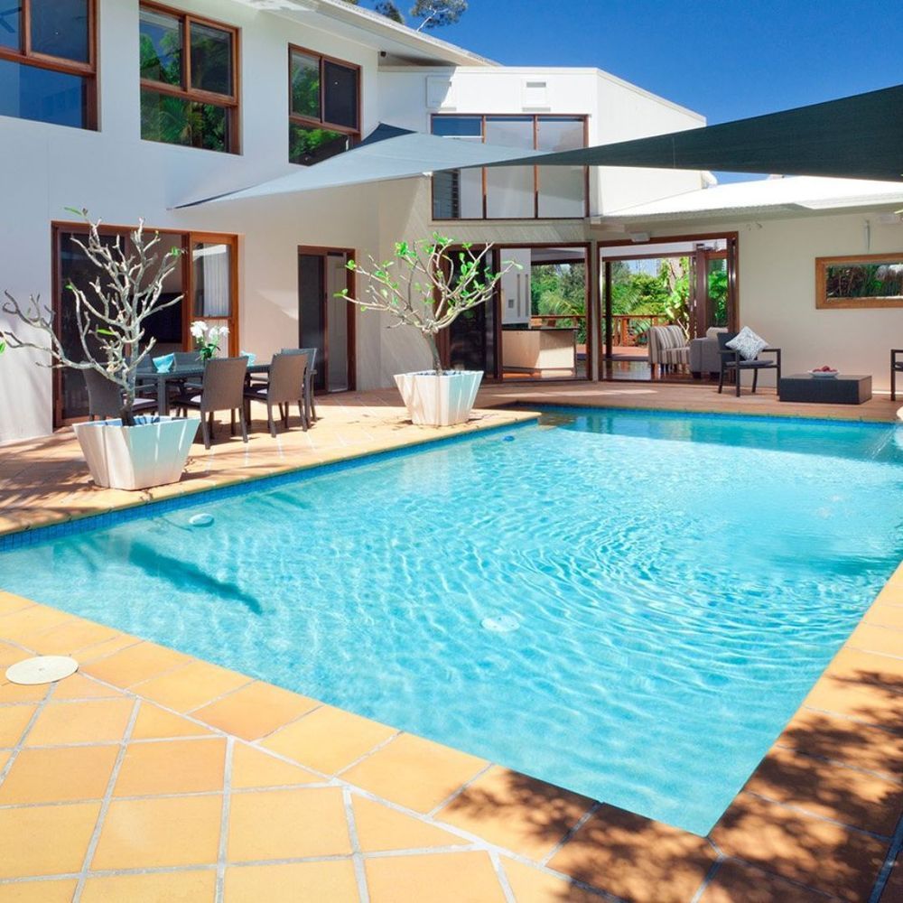 Modern house patio with a turquoise swimming pool and outdoor seating in bright sunlight
