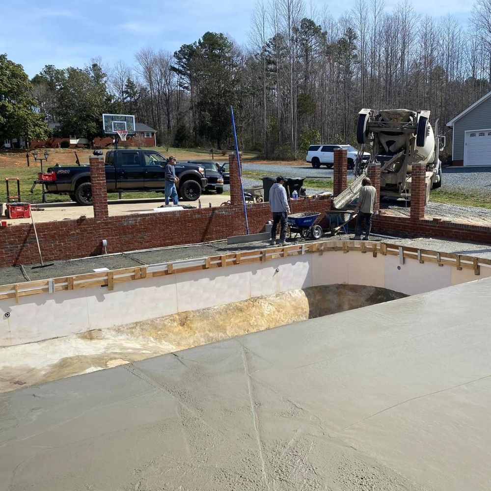 Pool construction site with workers pouring concrete beside a partially built in-ground pool.