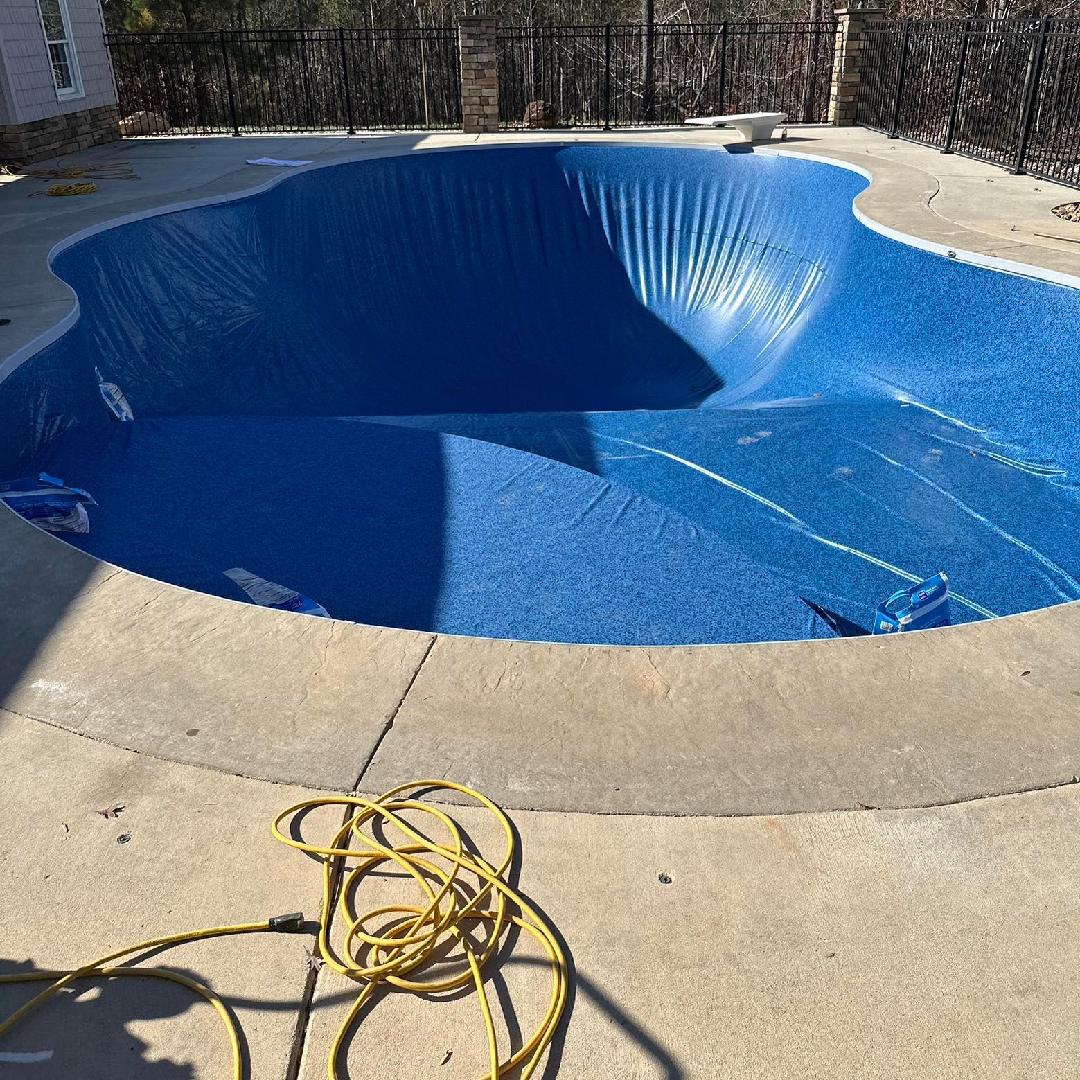 Empty blue swimming pool under repair, with coiled hose on the concrete deck.