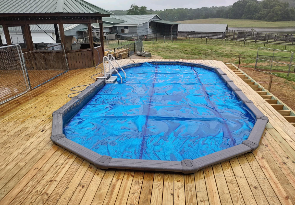 Covered blue pool on a wooden deck in a rural yard with a gazebo nearby