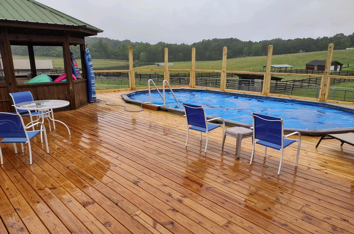 Rainy wooden deck beside blue pool and chairs overlooking a green landscape