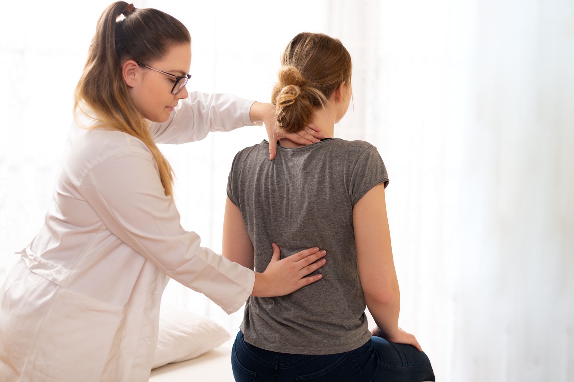 A healthcare professional examining a patient’s neck and back during a physical therapy session. A healthcare professional examining a patient’s neck and back during a physical therapy session.