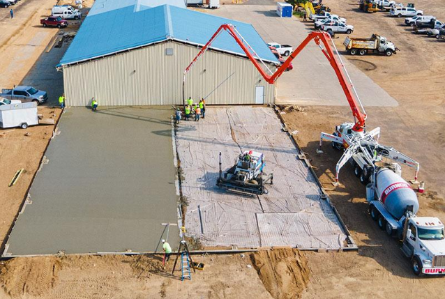 “Aerial view of a large concrete slab pour beside a warehouse with pump equipment by a concrete contractor in Casas Adobes, AZ”
