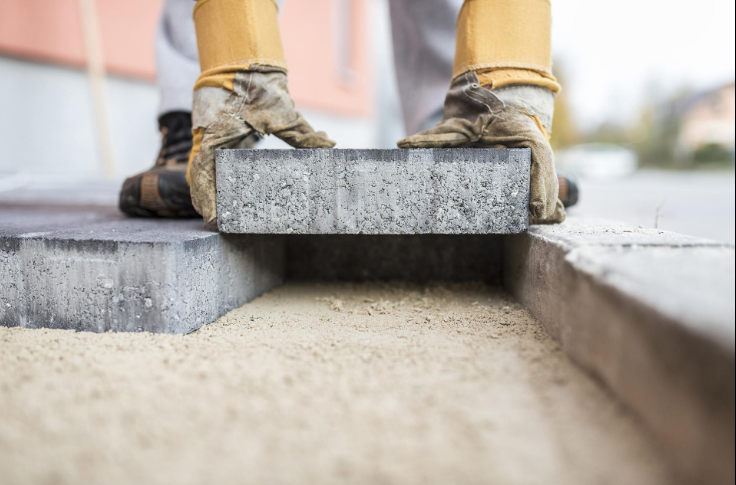 “Worker placing a large concrete paver into position for a clean walkway or patio surface by a concrete contractor in Casas Adobes, AZ”