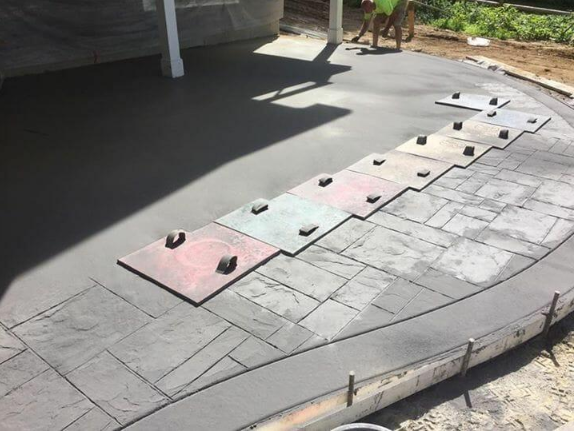 “Stamped concrete patio surface with decorative pattern work and sample boards during installation by a concrete contractor in Casas Adobes, AZ”