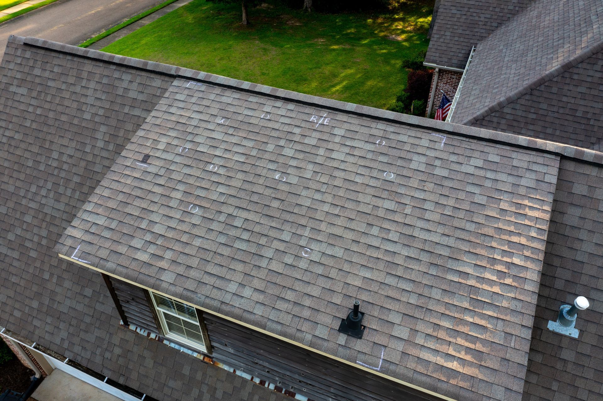 Aerial view of a gray-shingled house roof with two chimneys and a grassy yard nearby