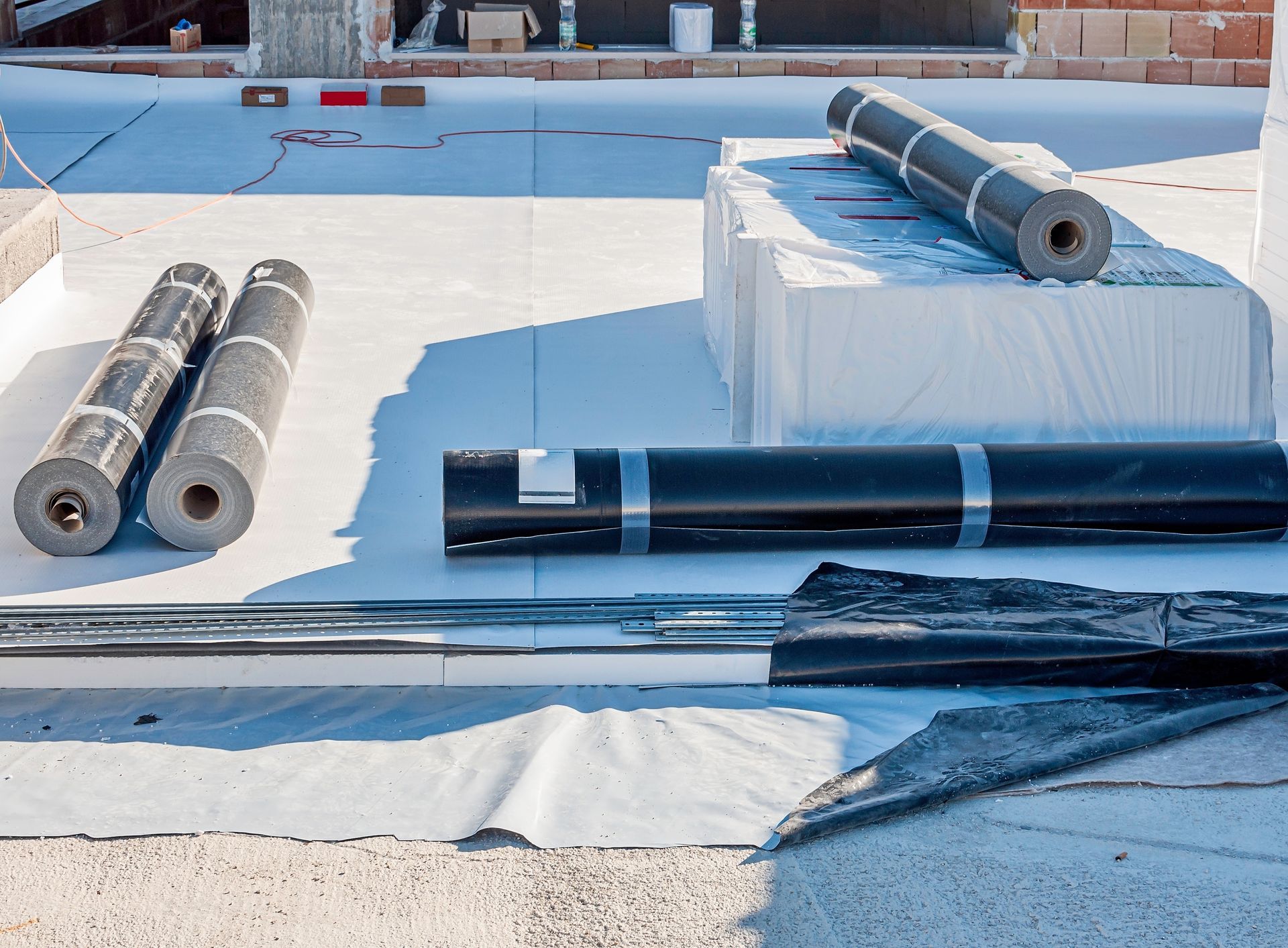 Bundles of metal pipes and shiny black rods stacked on white blocks in a bright outdoor industrial yard