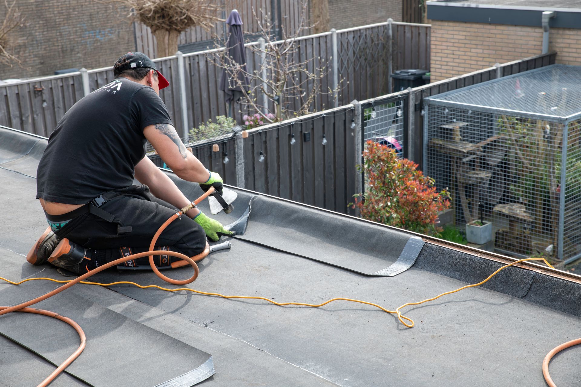 Worker pressure-washing a rooftop deck beside a fenced garden area