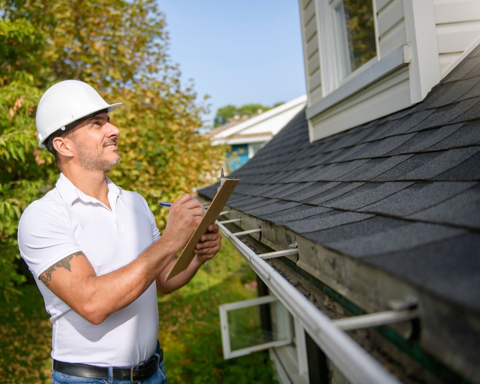 A man is standing on the roof of a house holding a clipboard.