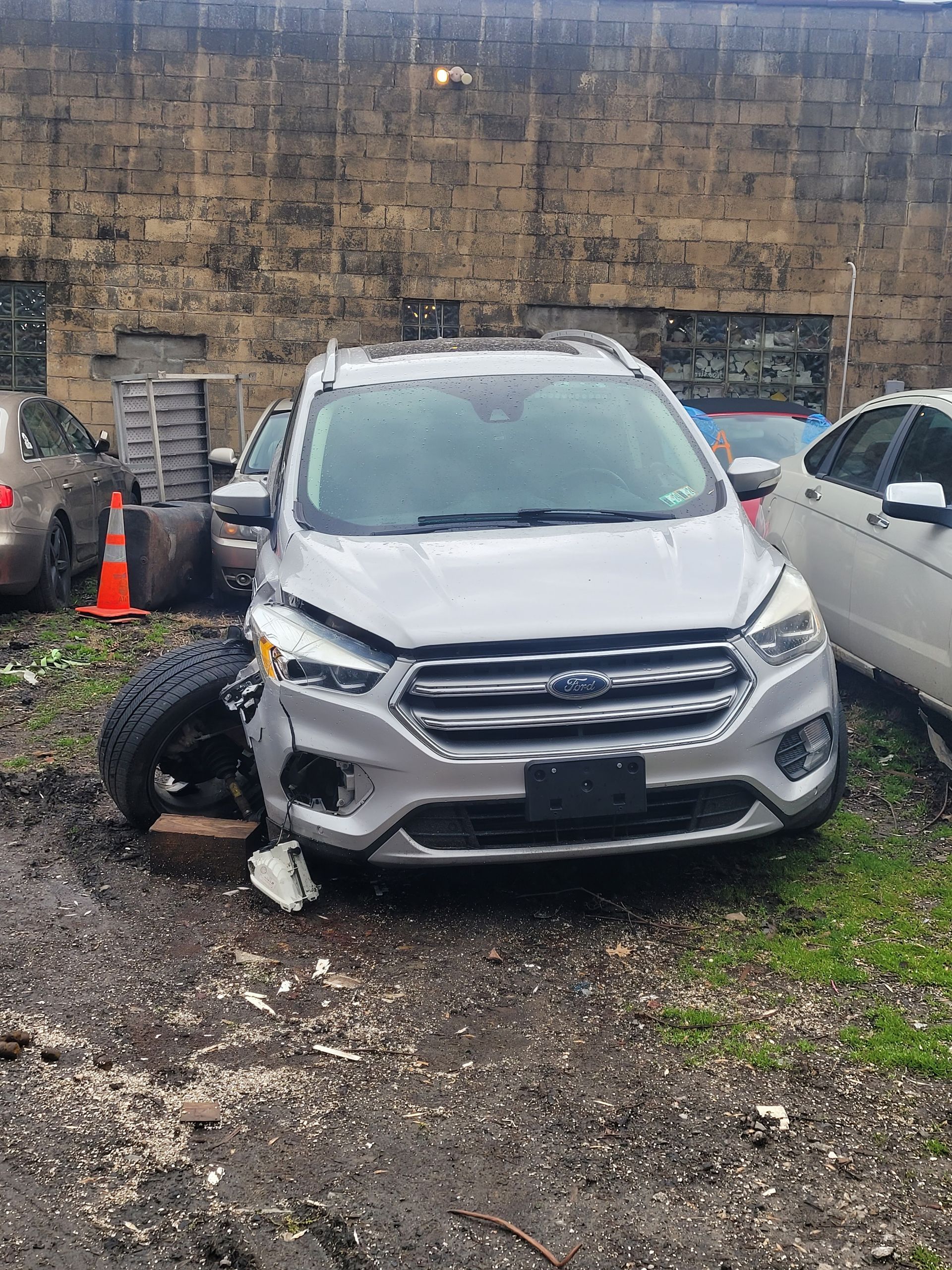 A white ford escape is parked in a lot with a broken tire.