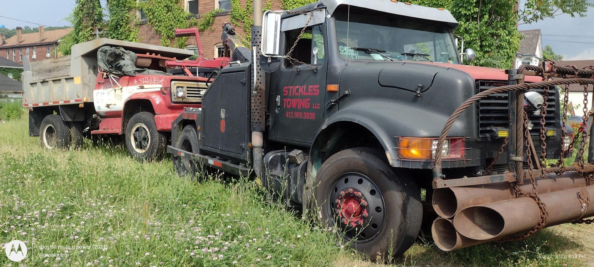 A tow truck is parked next to a dump truck in a field.