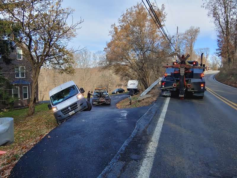 A white van is sitting on the side of the road next to a tow truck.