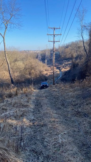A car is driving down a dirt road next to power lines.