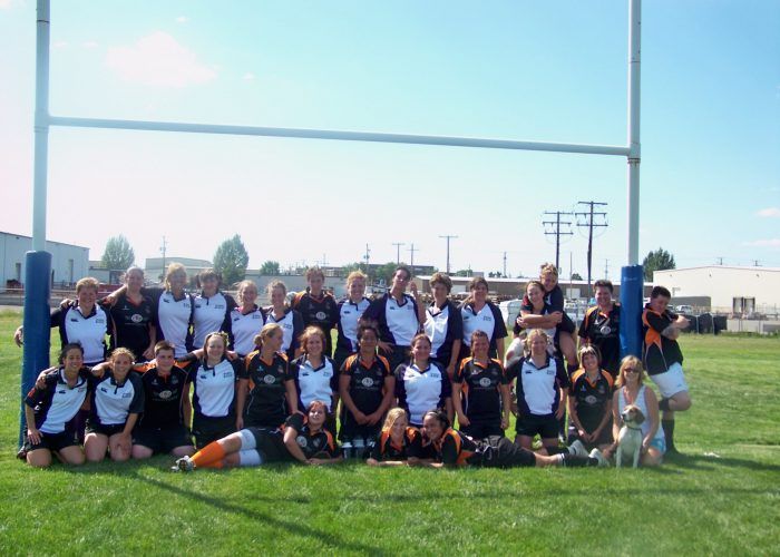A team of players in matching navy and white jerseys posing for a group photo on a grassy field under a goalpost.