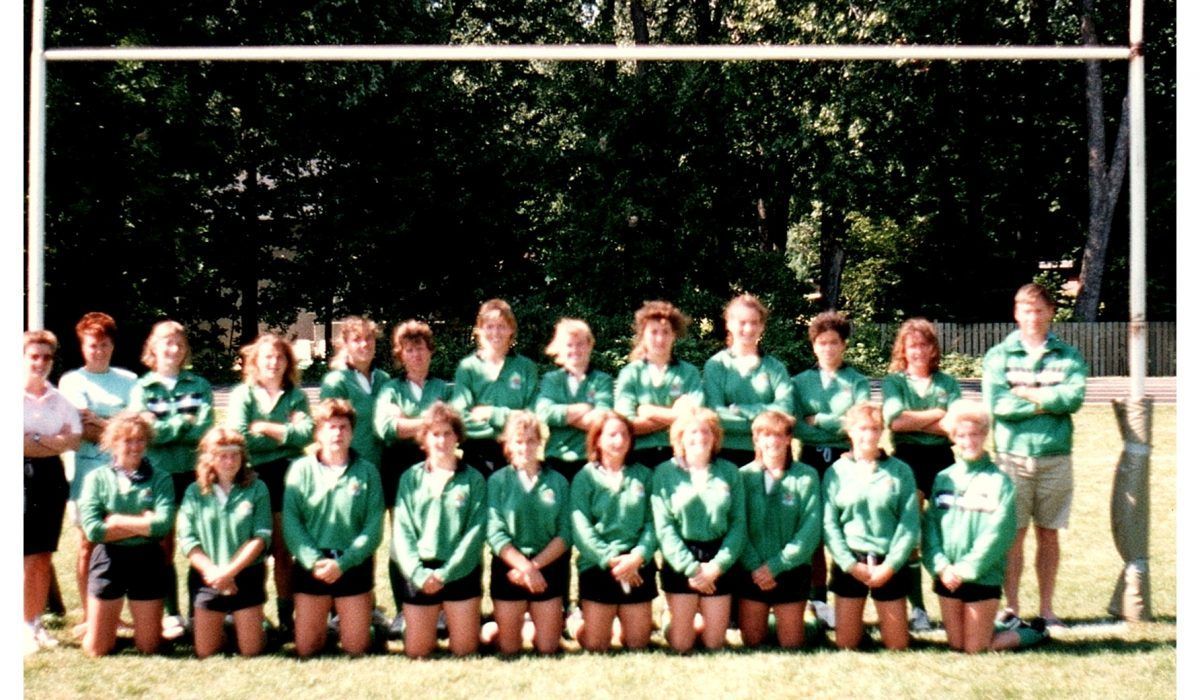 A team in matching green jackets and dark shorts poses for a group photo outdoors in front of a goalpost.
