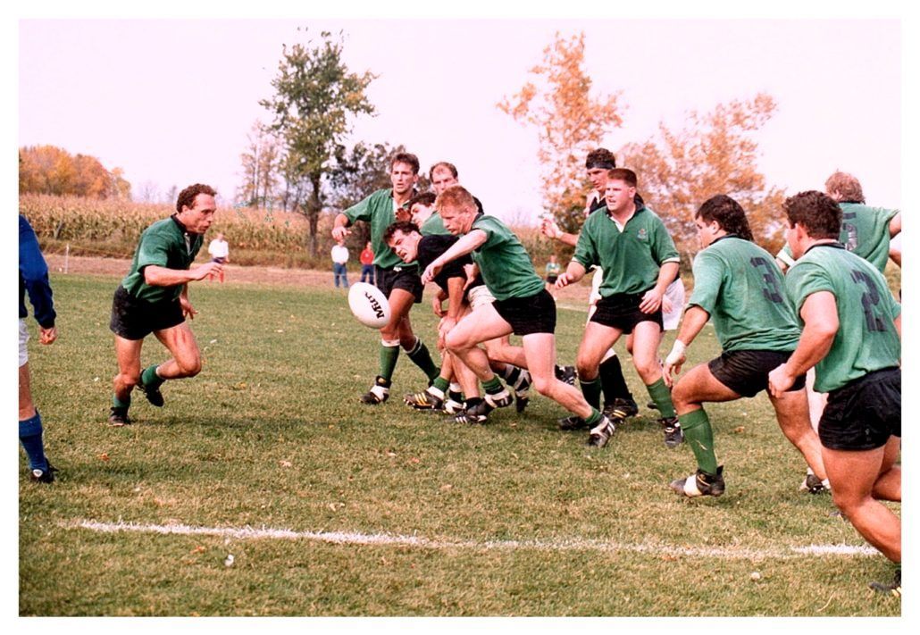 A group of rugby players in green jerseys competing for the ball on a grass field during a sunny outdoor game.