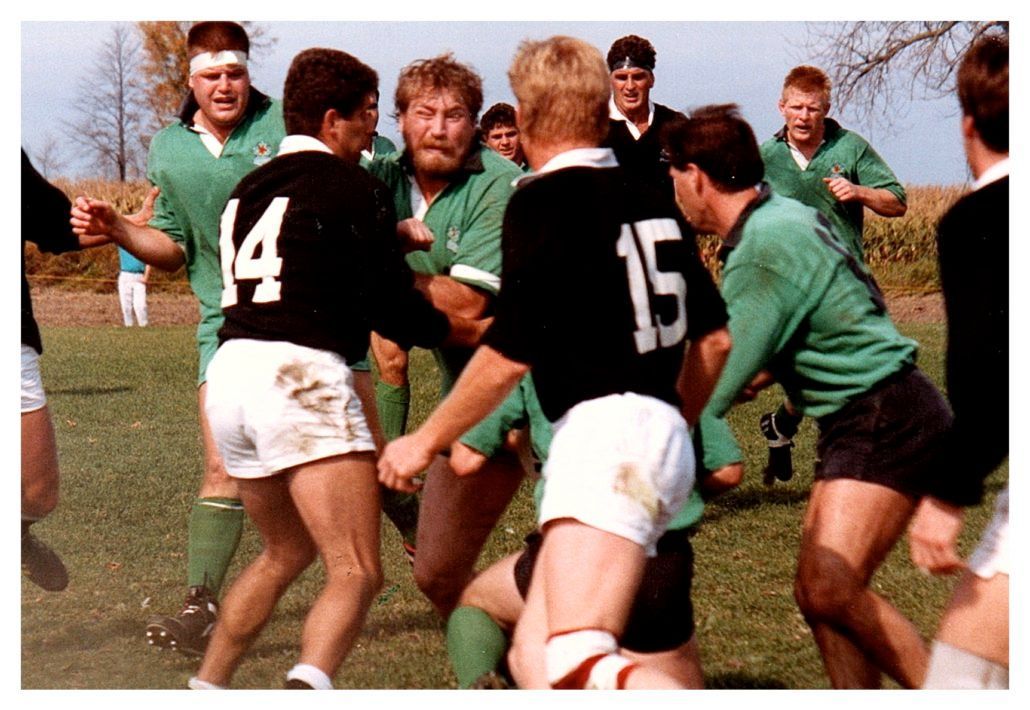 Rugby players in black and green uniforms compete on a grassy field during a match.
