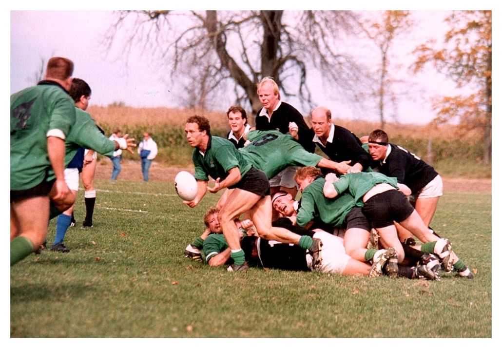 Rugby players in green and black jerseys compete for the ball during a match on an outdoor grass field.