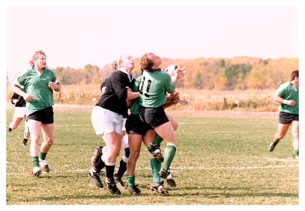 Rugby players in green and black uniforms compete for a ball during a match on an outdoor field.