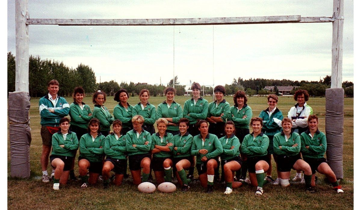 A team of players in matching green jerseys and shorts poses for a group photo in front of a rugby goalpost.