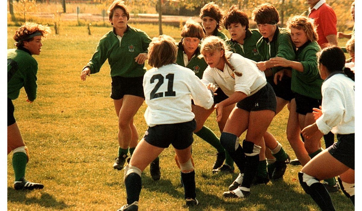 A rugby game in progress with players in green and white jerseys competing for possession on a grassy field.