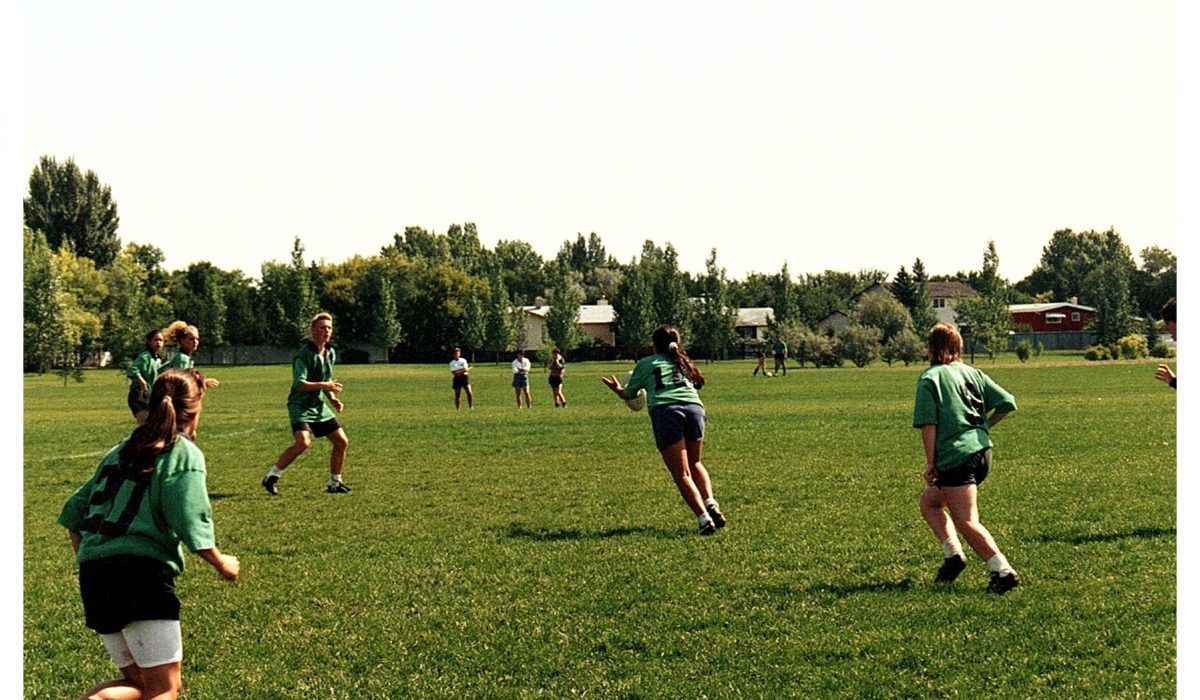 Several people in green jerseys run across a grass field during a sunny outdoor game.