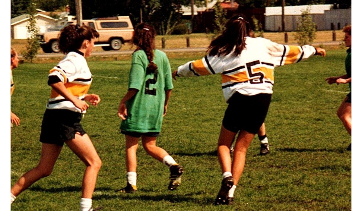 Several players run across a sunny grassy field during a casual soccer game.