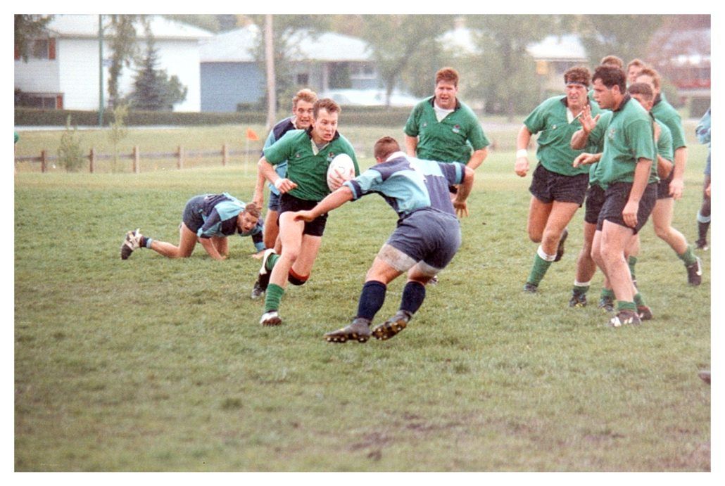 Rugby players in green and light blue uniforms compete on a field during a match.