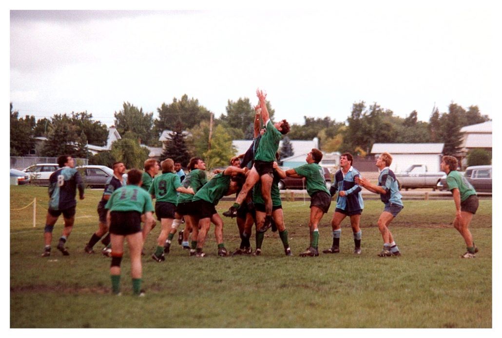 Rugby players in green and blue jerseys contest a ball in a lineout on a grassy field.