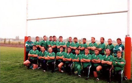 A group of rugby players in green uniforms posing for a team photo on a field in front of a goalpost.