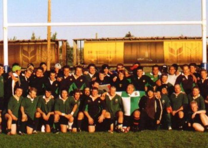 A large group of rugby players in green and black jerseys pose together on a field in front of a train car.