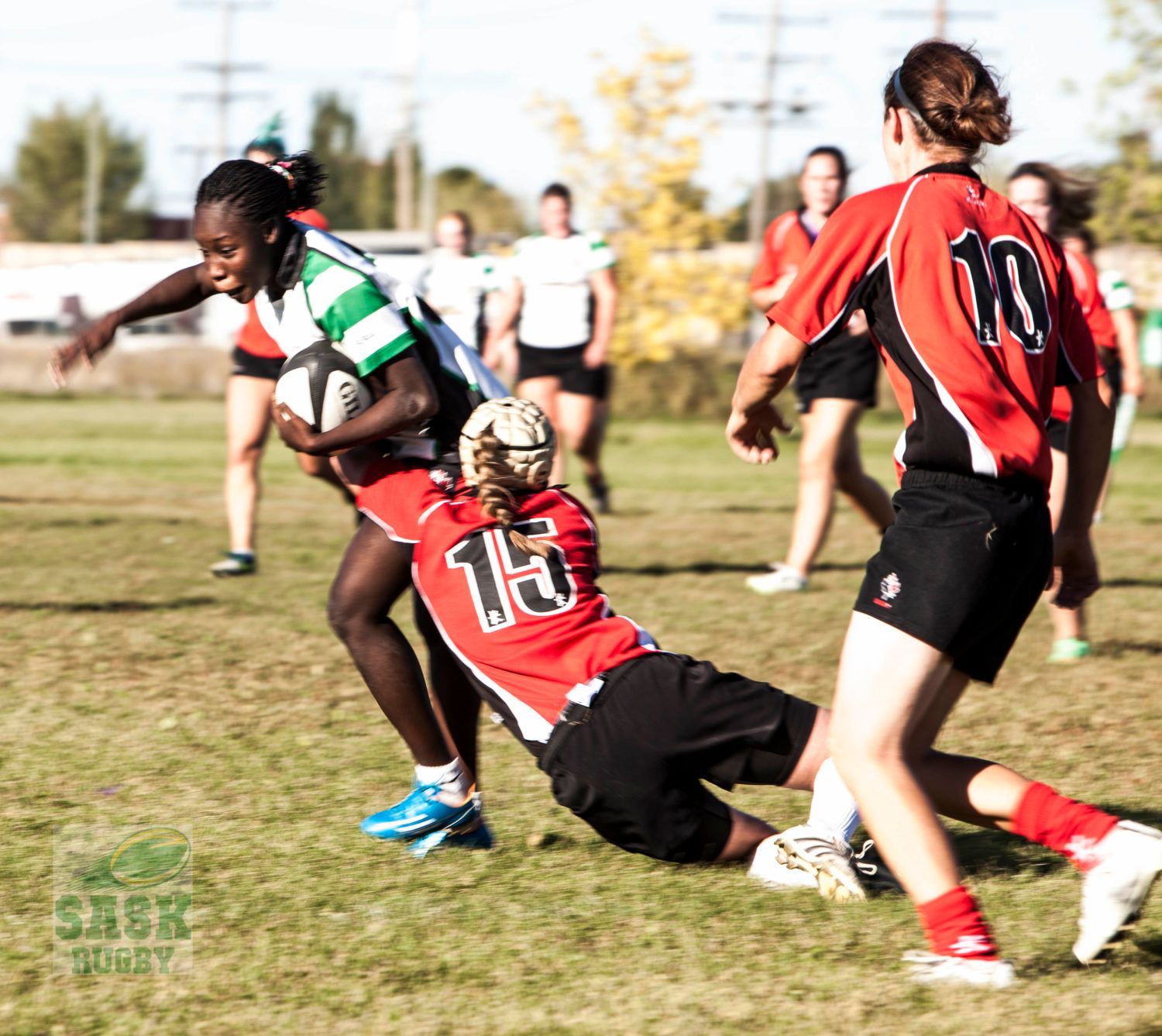 A rugby player in a green and white jersey runs with the ball while being tackled by a player in a red jersey.
