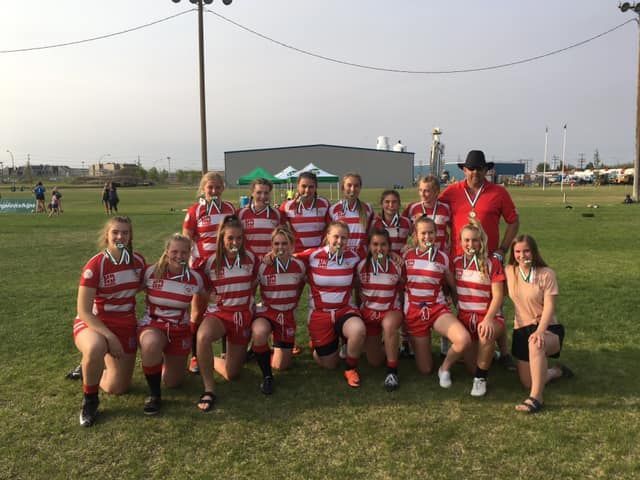 A team in red and white striped jerseys stands on a grassy field, posing for a photo after a competition.