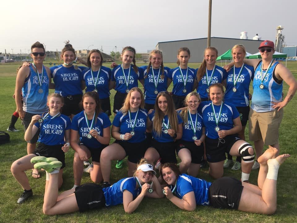 A group of rugby players in blue uniforms and medals pose for a photo on a grassy field.