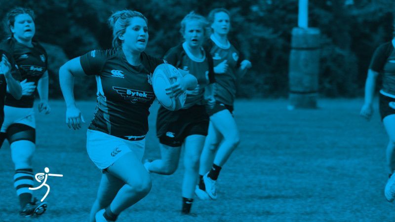 A rugby player runs across a field holding the ball, followed by teammates. A blue color filter is applied over the scene.
