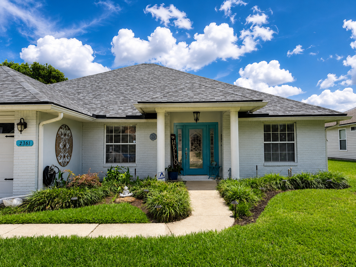 Single-story white house with teal front doors, gray roof, and a manicured lawn under a blue sky