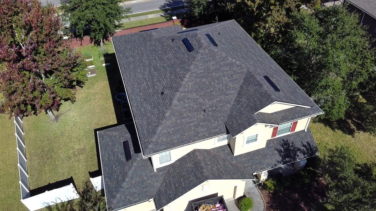 Aerial view of a gray-roofed house with a driveway and trees surrounding it