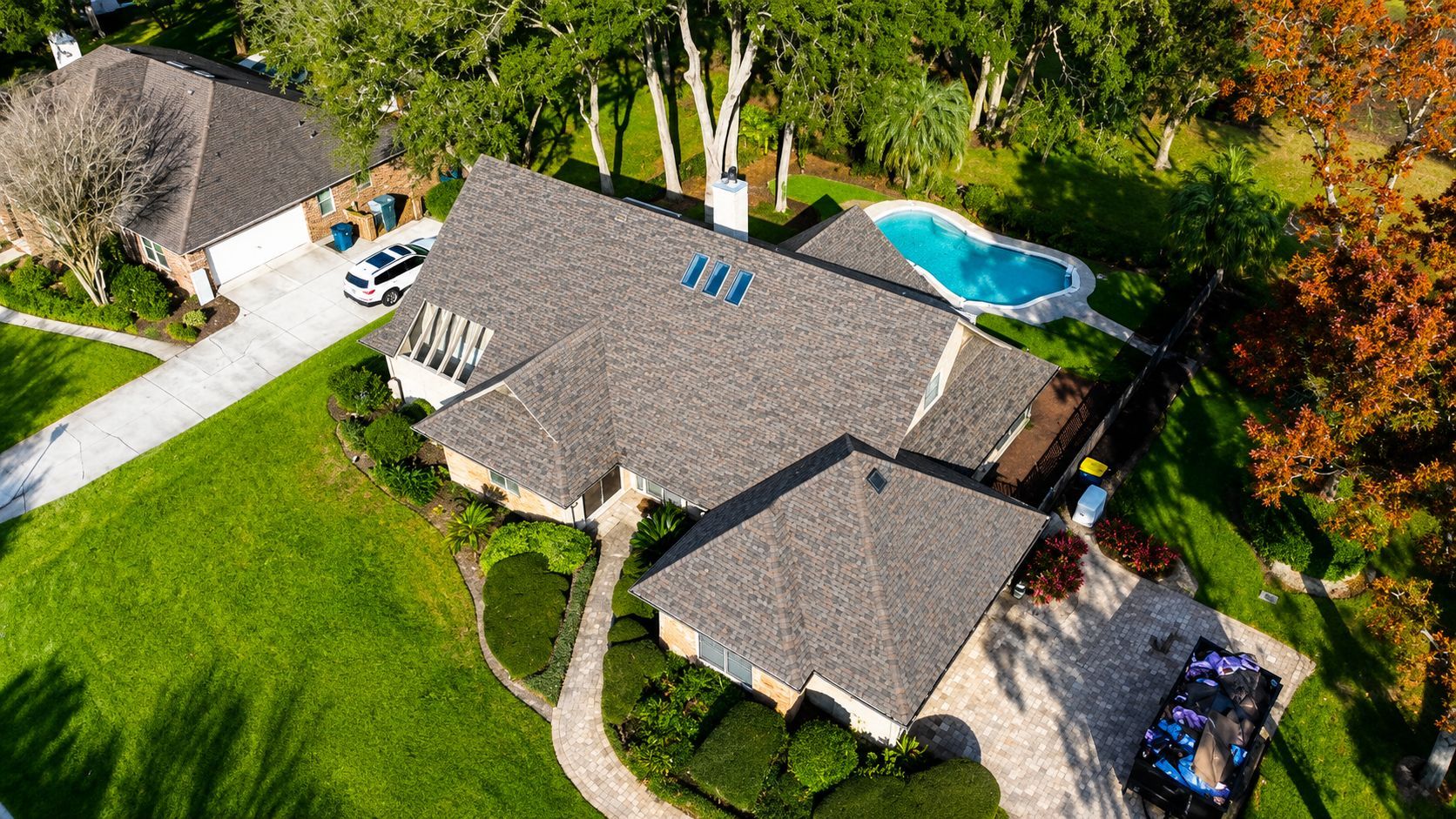 Aerial view of a house with a gray roof, green lawn, driveway, and a backyard pool.