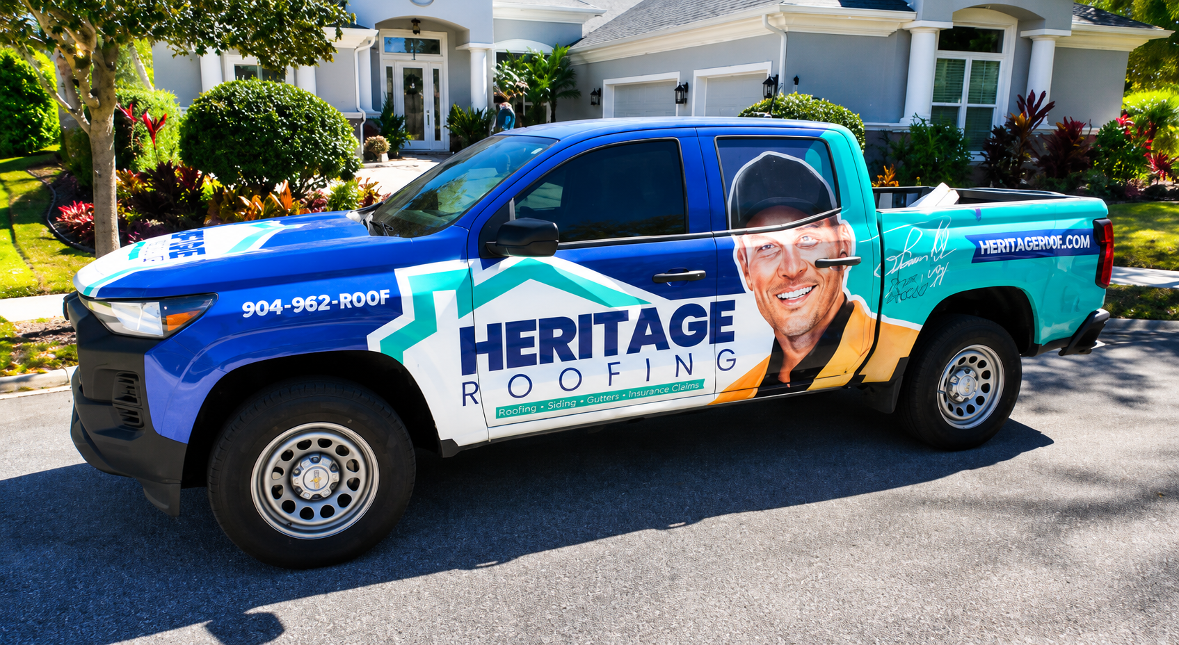 A worker in protective gear uses a nail gun to install asphalt shingles on a sloped roof.