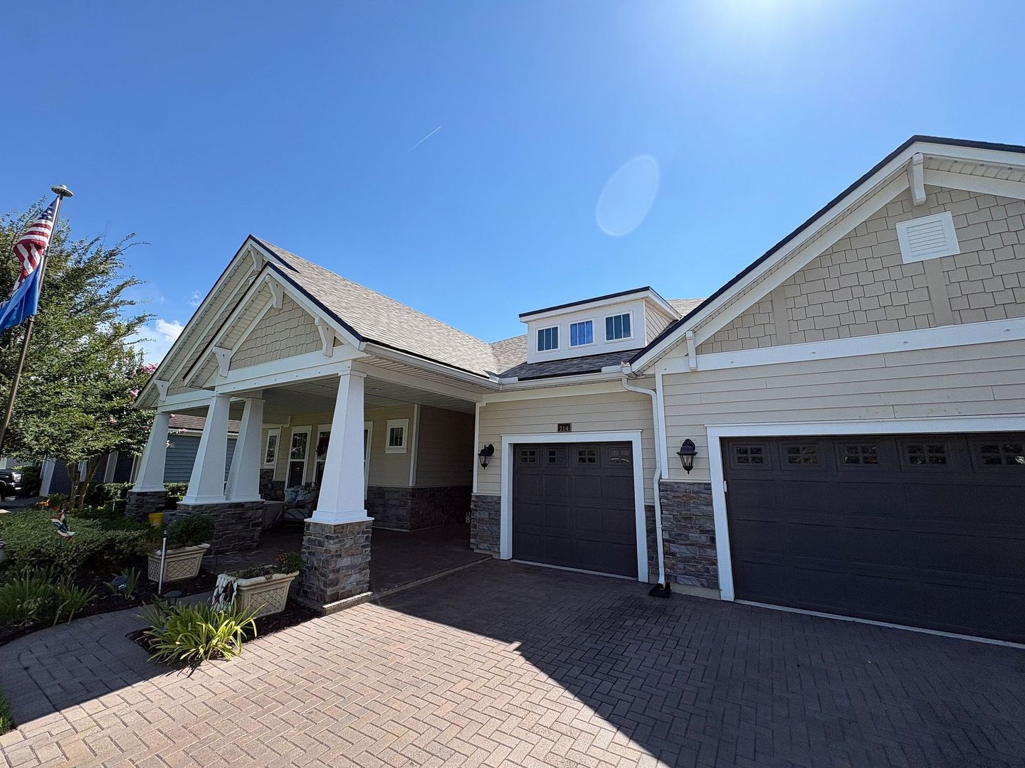 Large beige suburban house with a covered entry and two-car garage under a bright blue sky