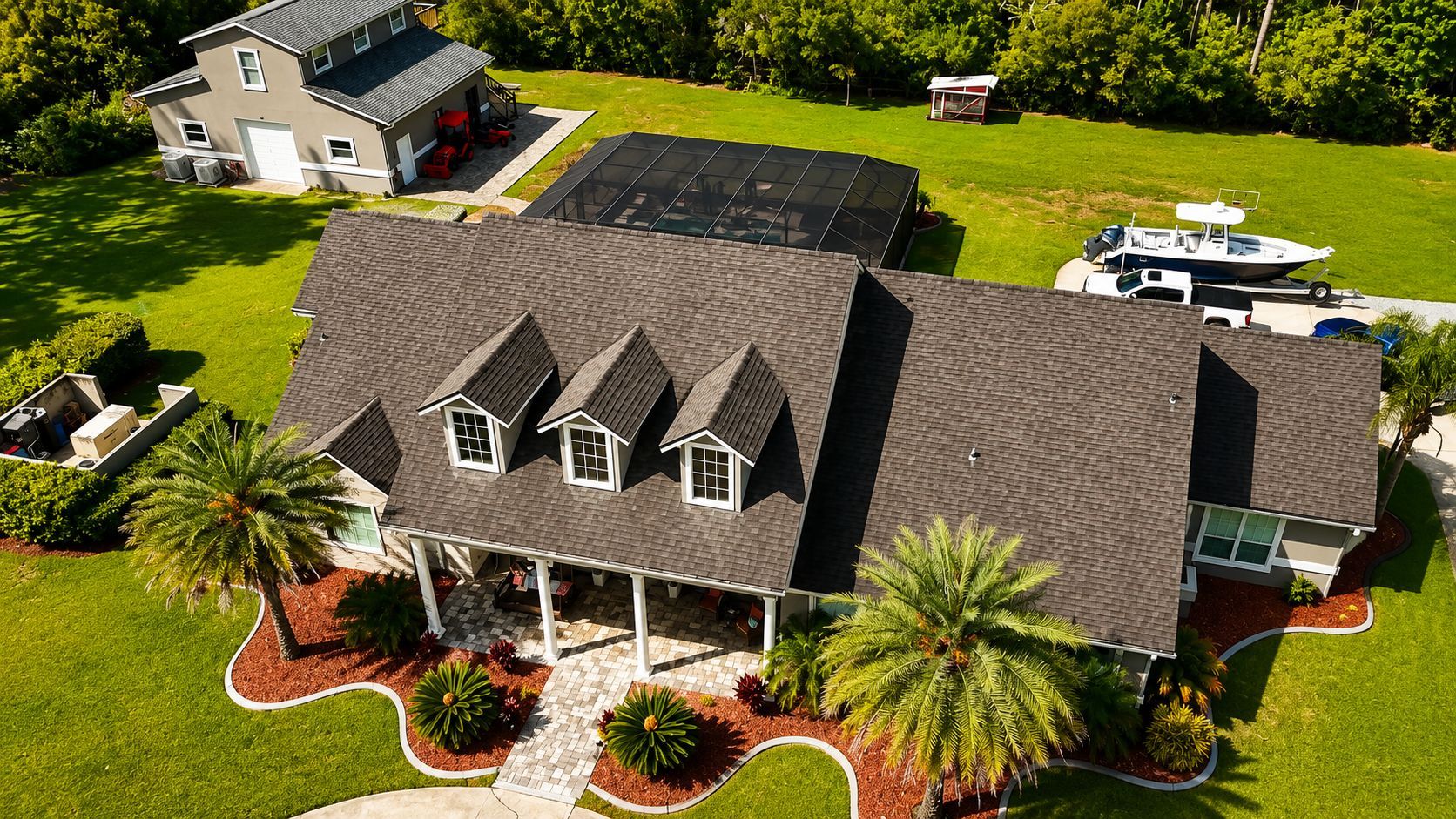 Aerial view of a house with a dark roof, manicured lawn, and palm trees in the front yard.