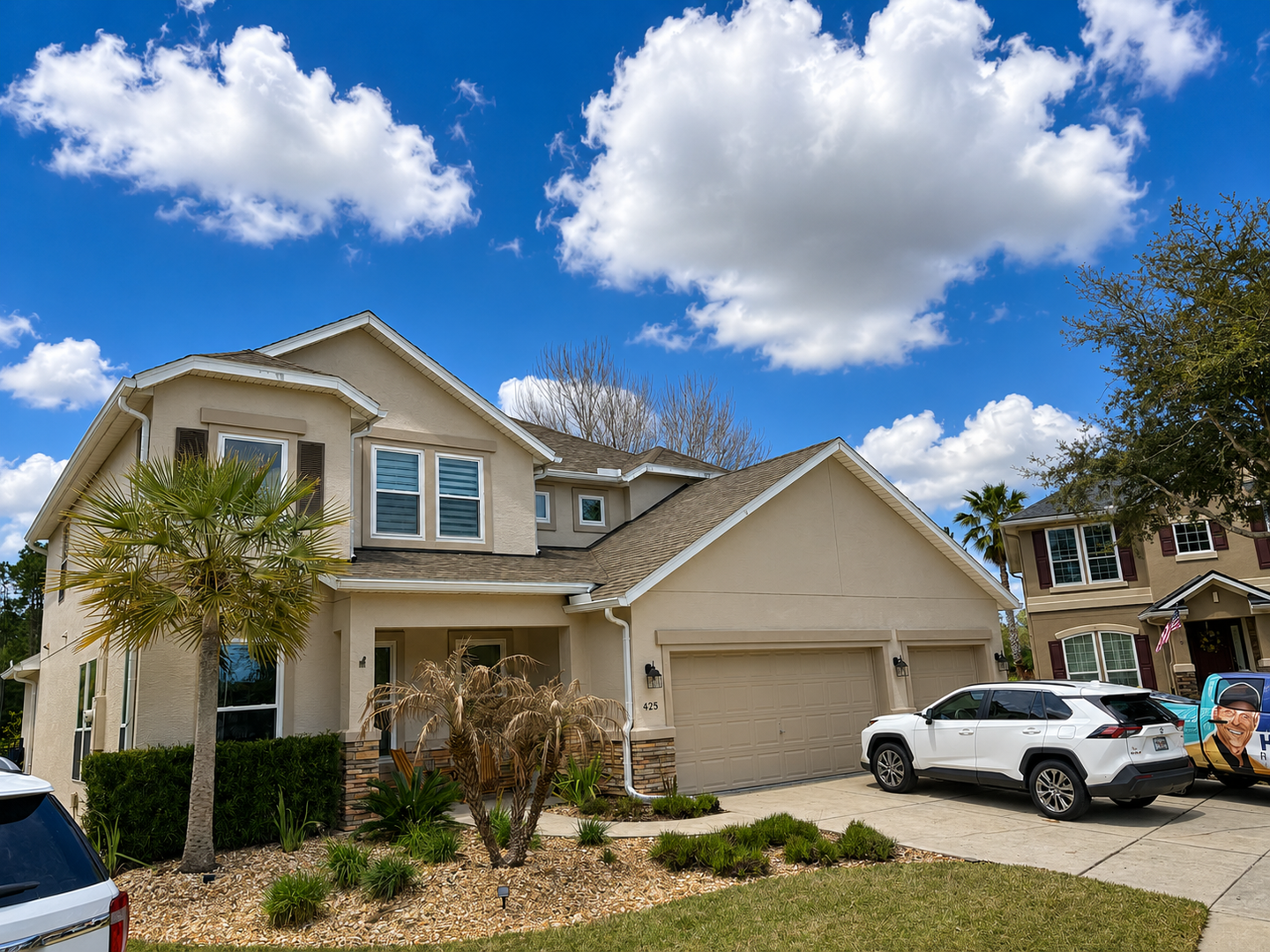Suburban two-story house with white SUV in driveway under a blue sky with clouds