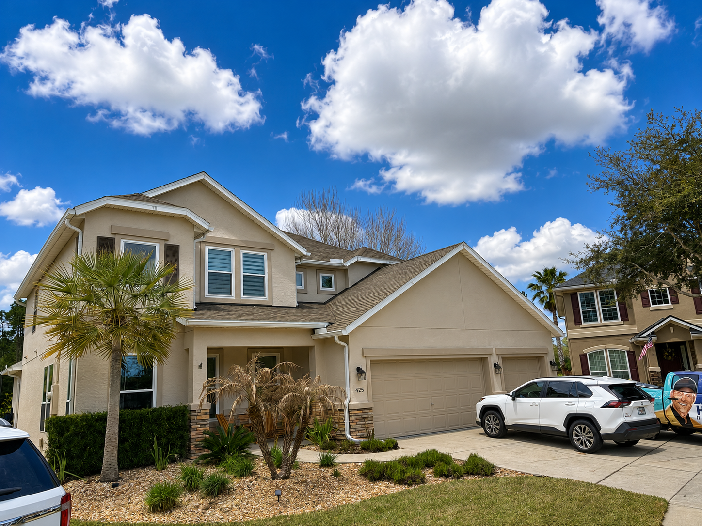 Suburban two-story house with white SUV in driveway under a blue sky with clouds