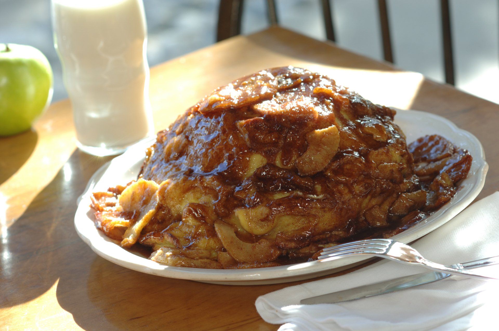 Apple pancake covered in caramelized apples on a plate next to milk and an apple on a table.