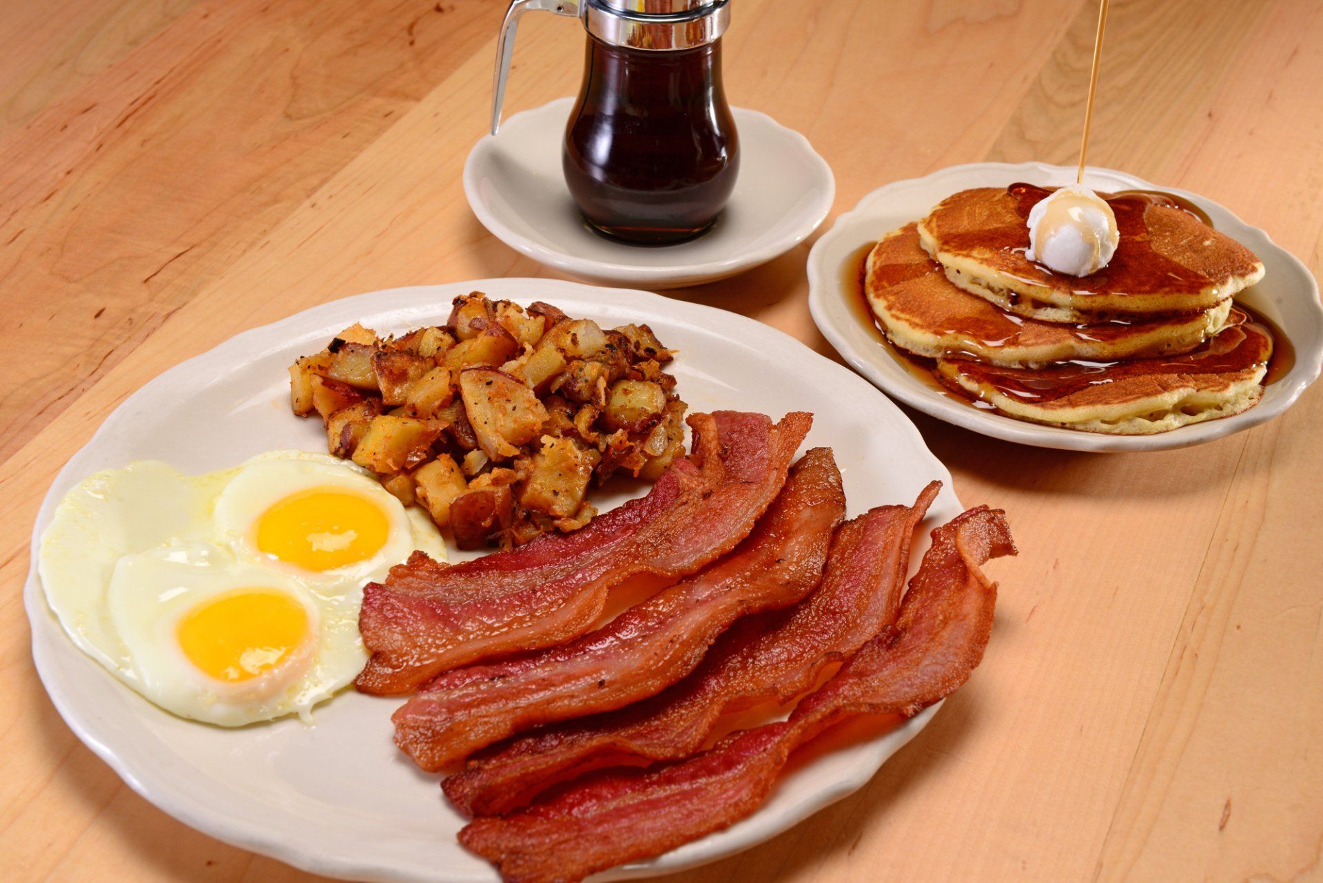 Breakfast plate with eggs, bacon, potatoes, and pancakes with syrup.