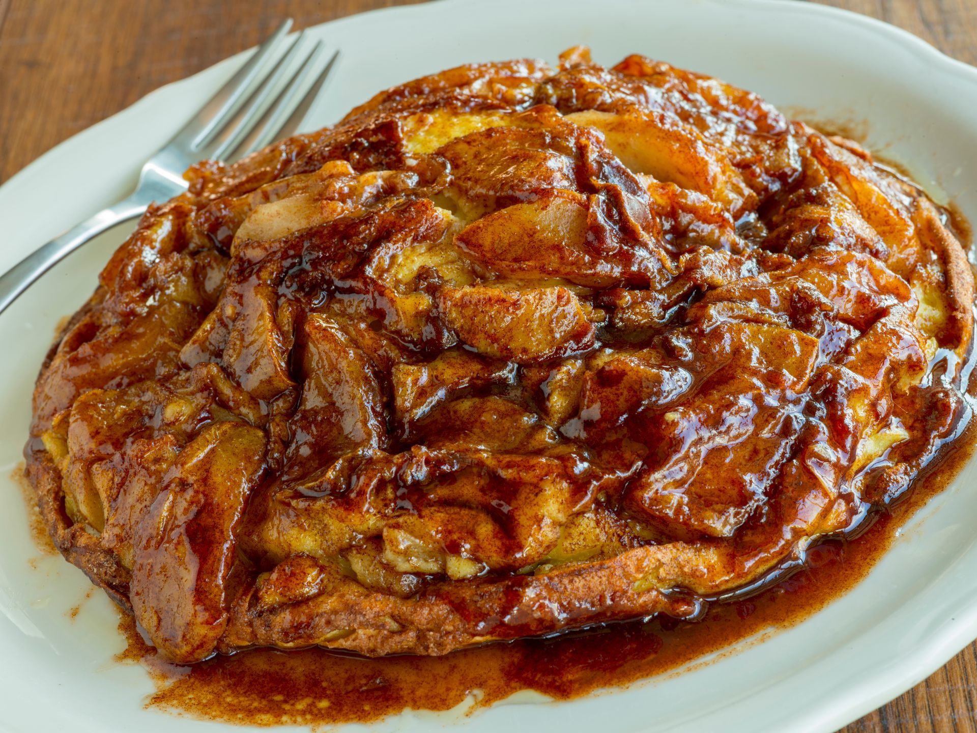 Apple upside-down cake on a white plate with a fork. Glazed, caramelized apples on top.