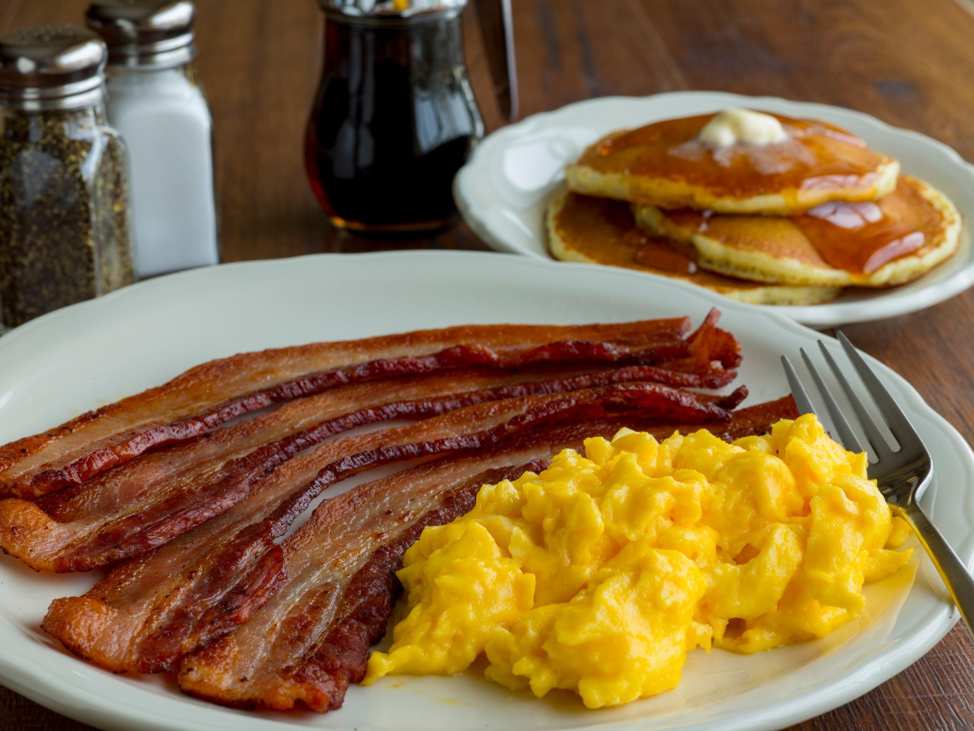 Breakfast plate with bacon, scrambled eggs, and pancakes with syrup.